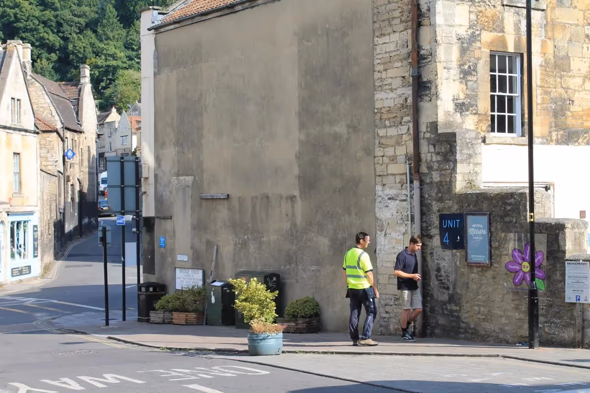 Two workers standing on stone street near old buildings and Unit 4 sign