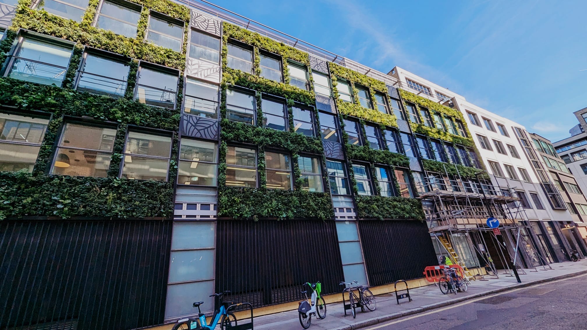 Green-covered modern office building with glass windows and bicycles parked outside