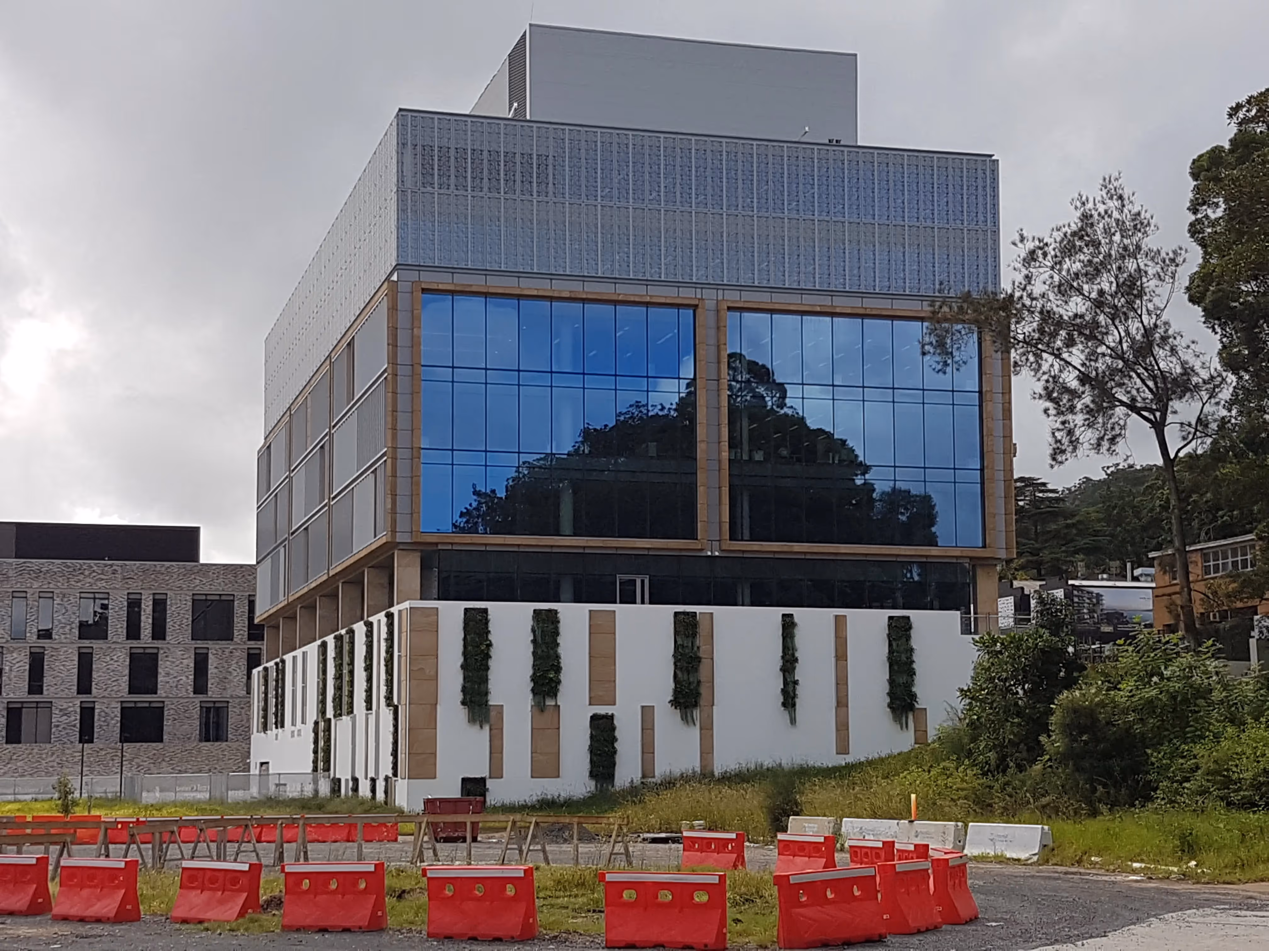 Modern glass building with vertical gardens, surrounded by red construction barriers