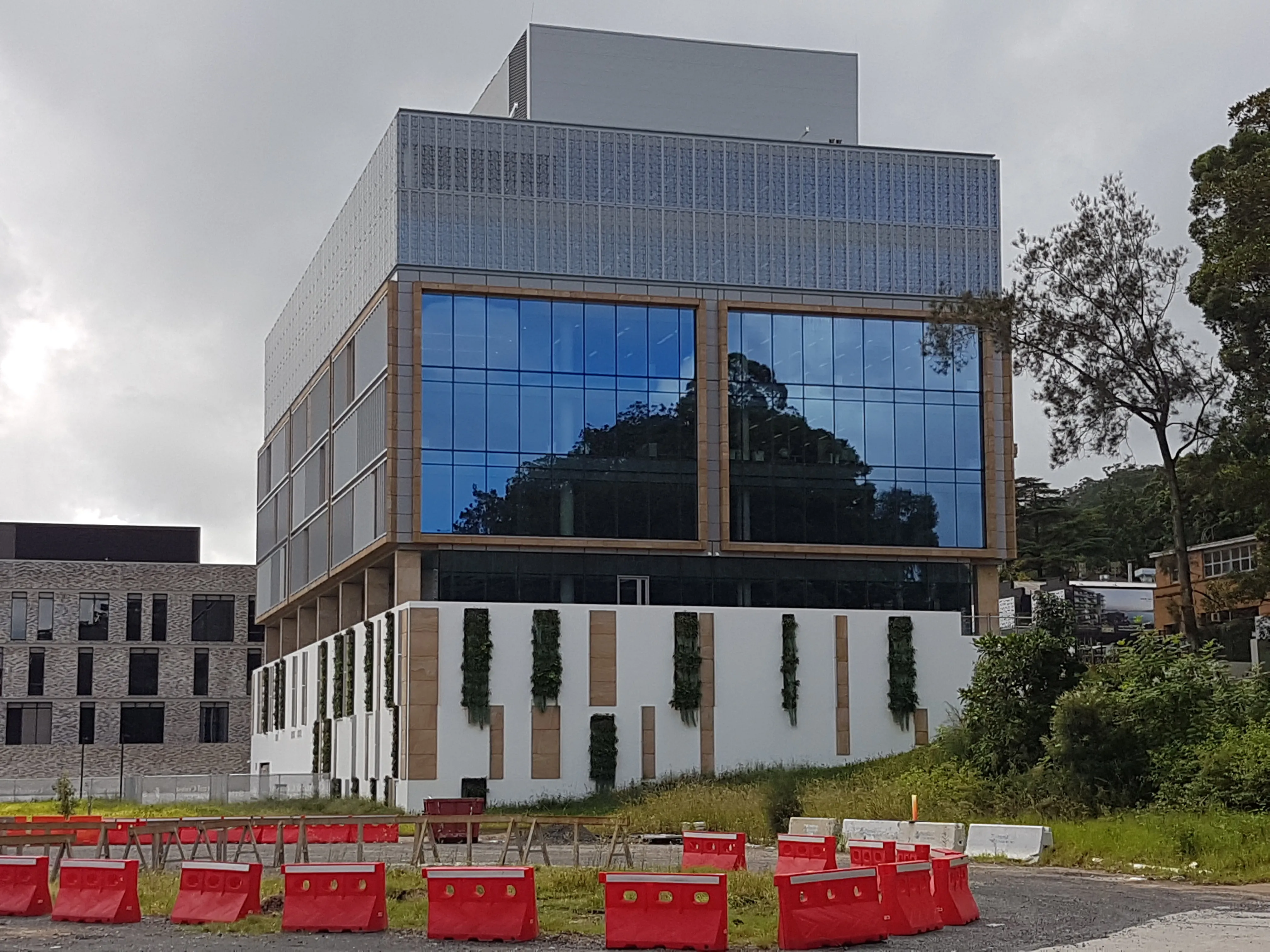 Modern glass building with vertical gardens, surrounded by red construction barriers