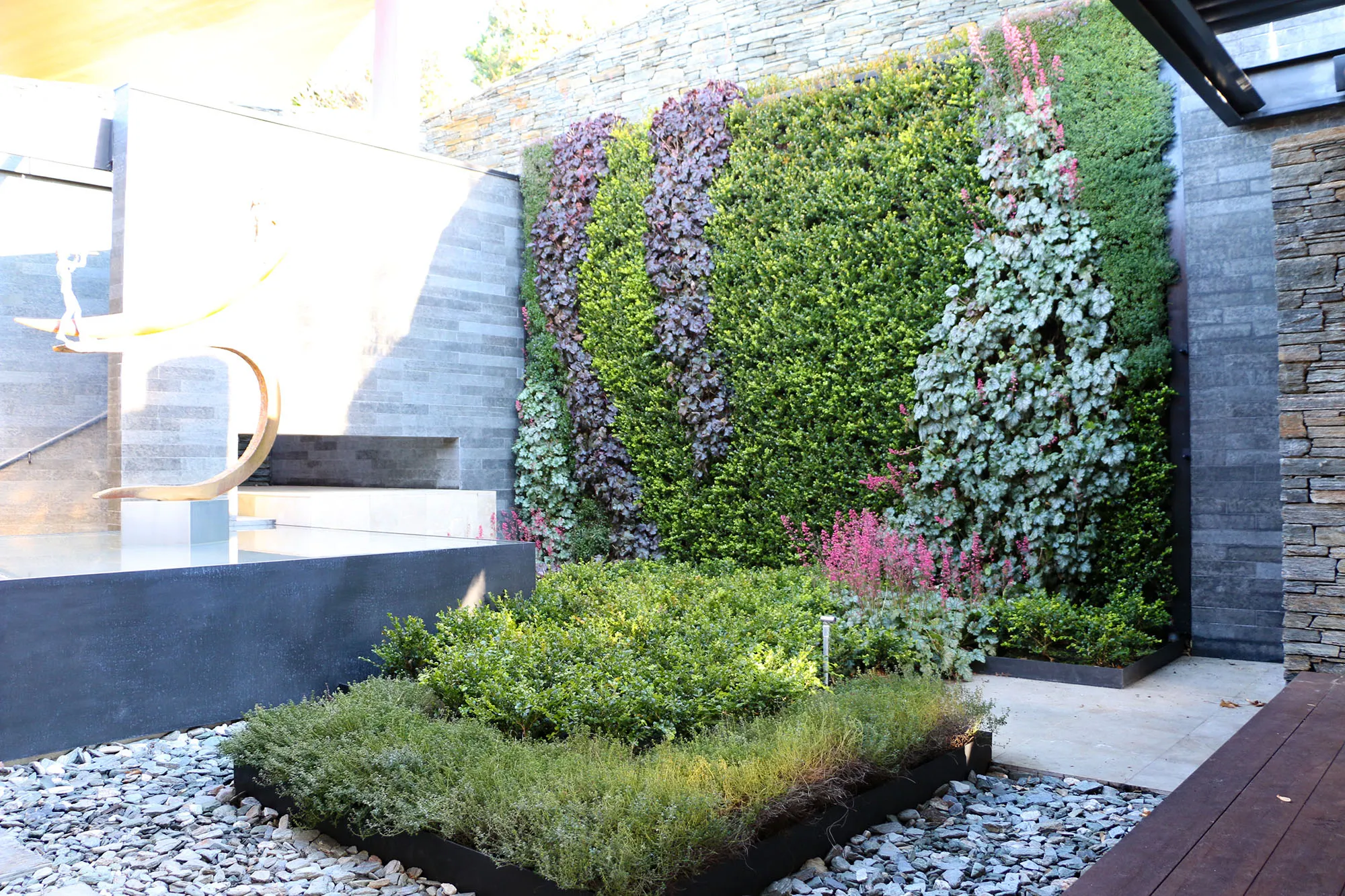 Modern vertical garden with colorful plants on stone wall, surrounded by rocks