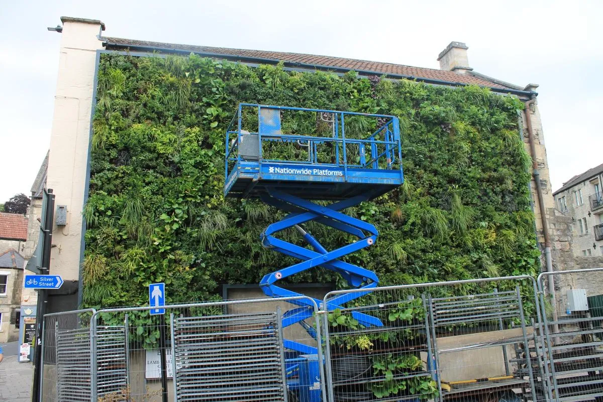 Blue scissor lift platform on green living wall with street sign