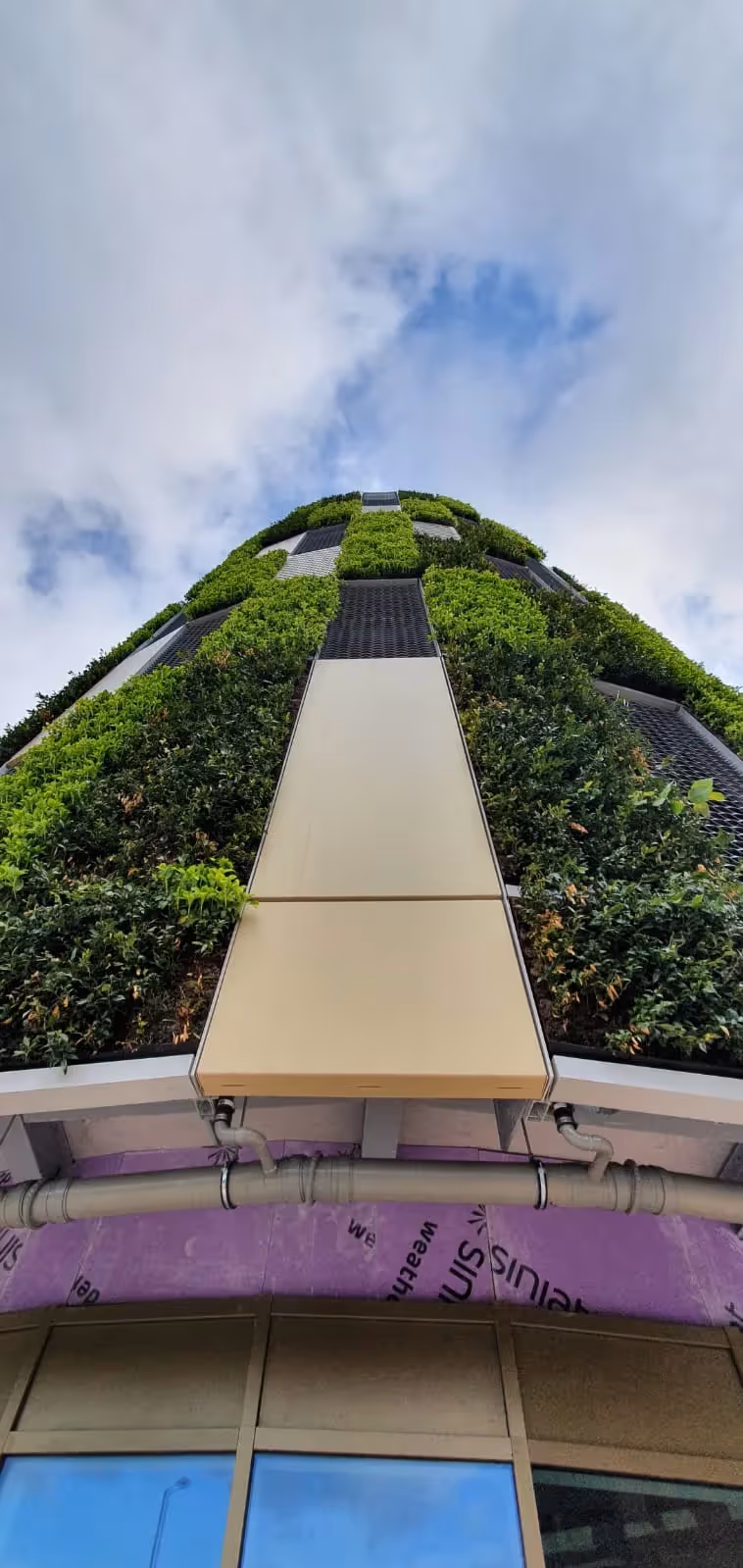 Green vertical garden covering modern building with walkway against cloudy sky