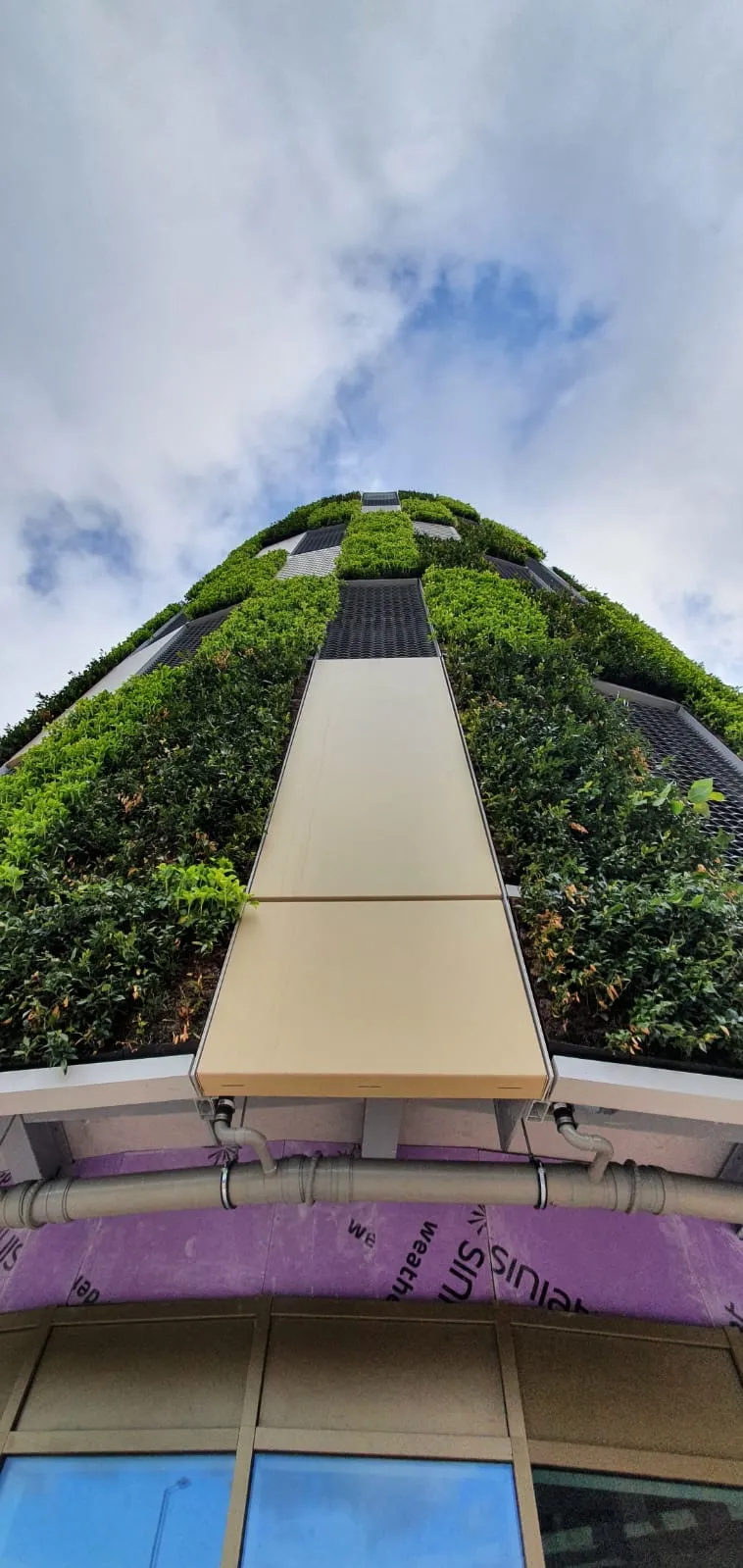 Green vertical garden covering modern building with walkway against cloudy sky