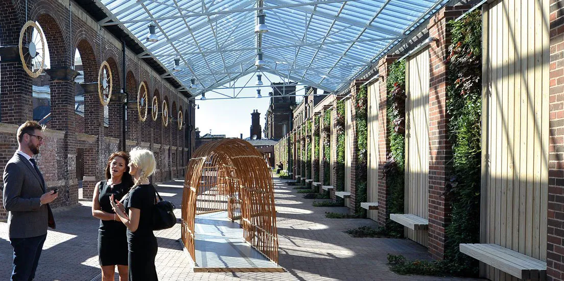 Glass-roofed corridor with people, wooden arch, and vertical gardens