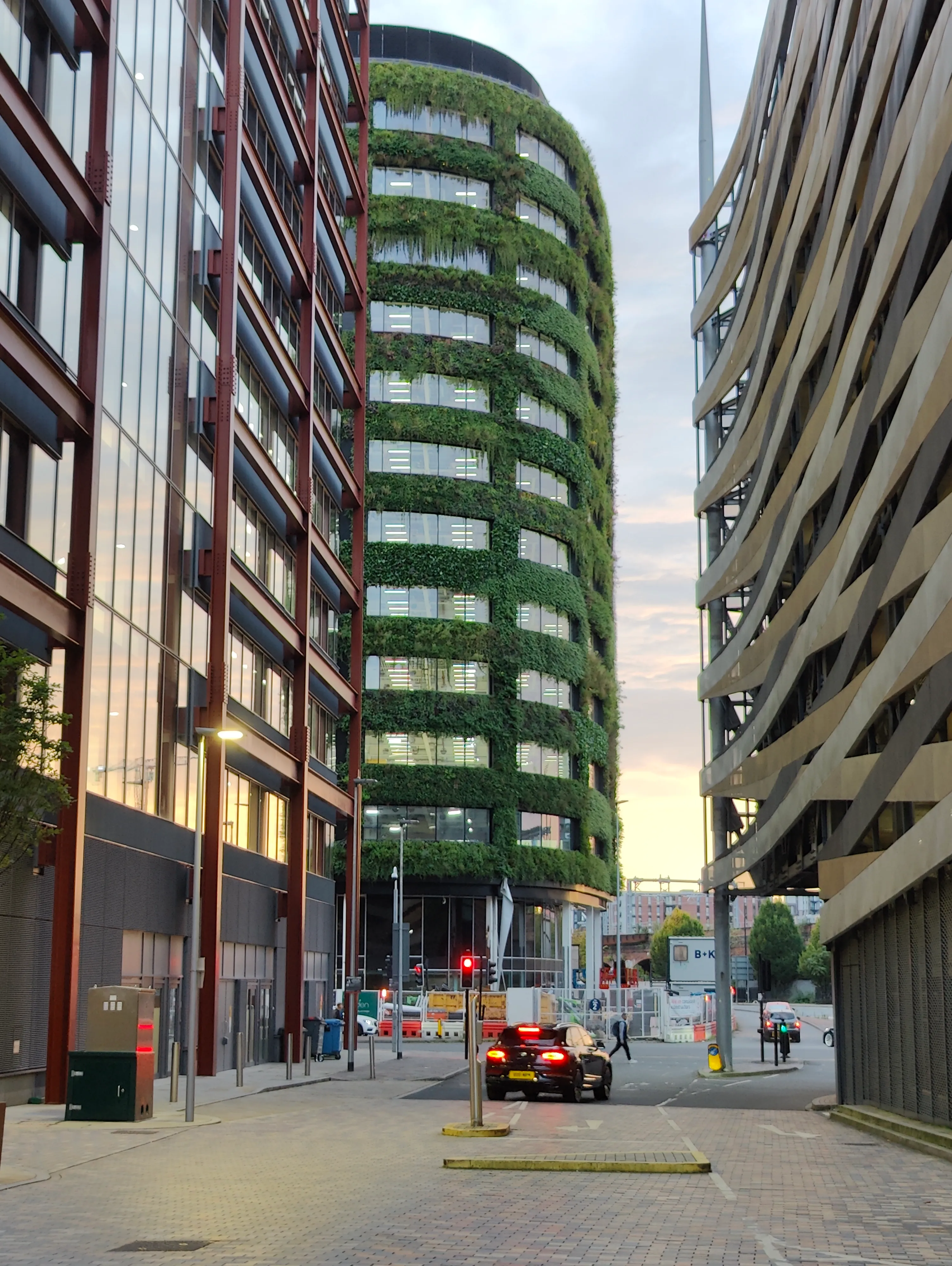 Green-covered circular building among modern urban architecture with street scene