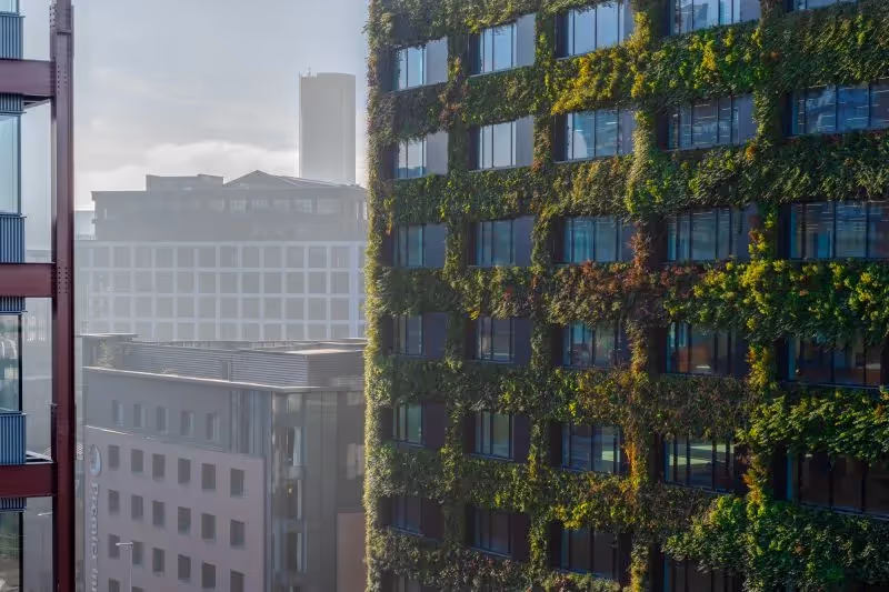 Green-covered modern office building with vertical garden among urban skyline