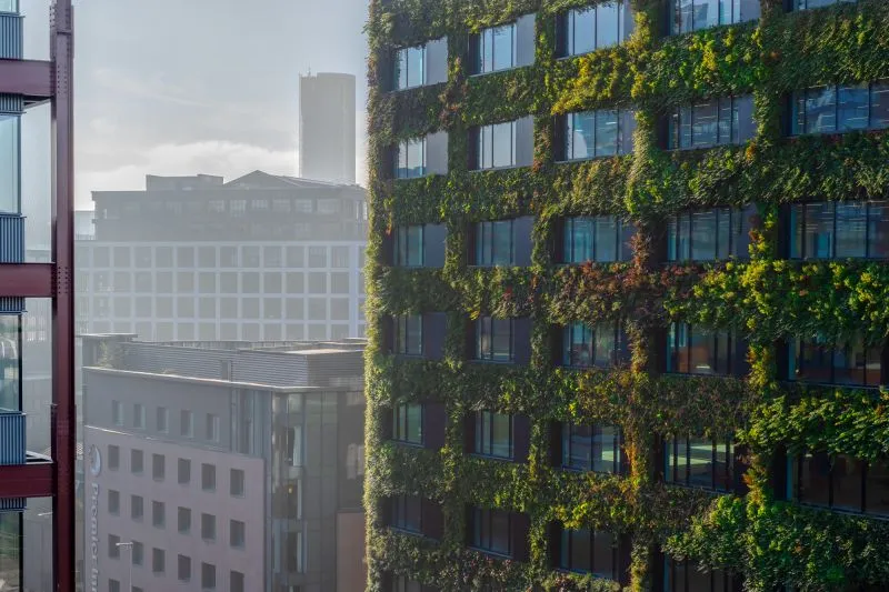 Green-covered modern office building with vertical garden among urban skyline