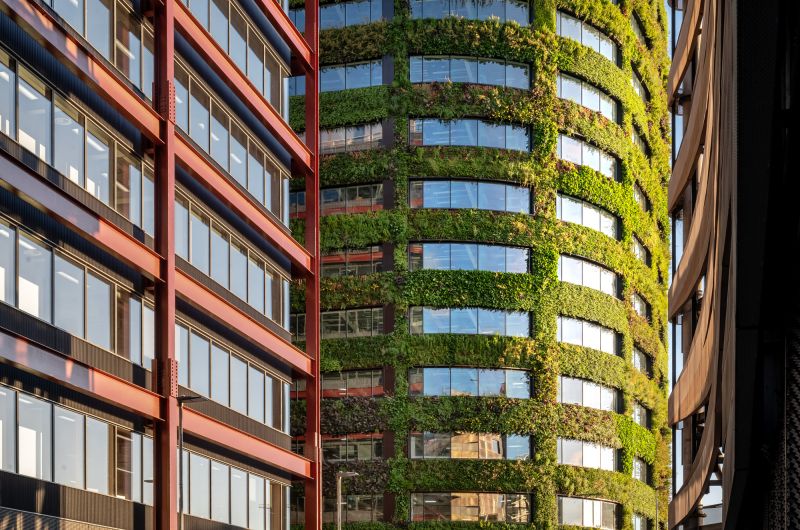 Curved green-covered skyscraper with glass windows next to red brick building