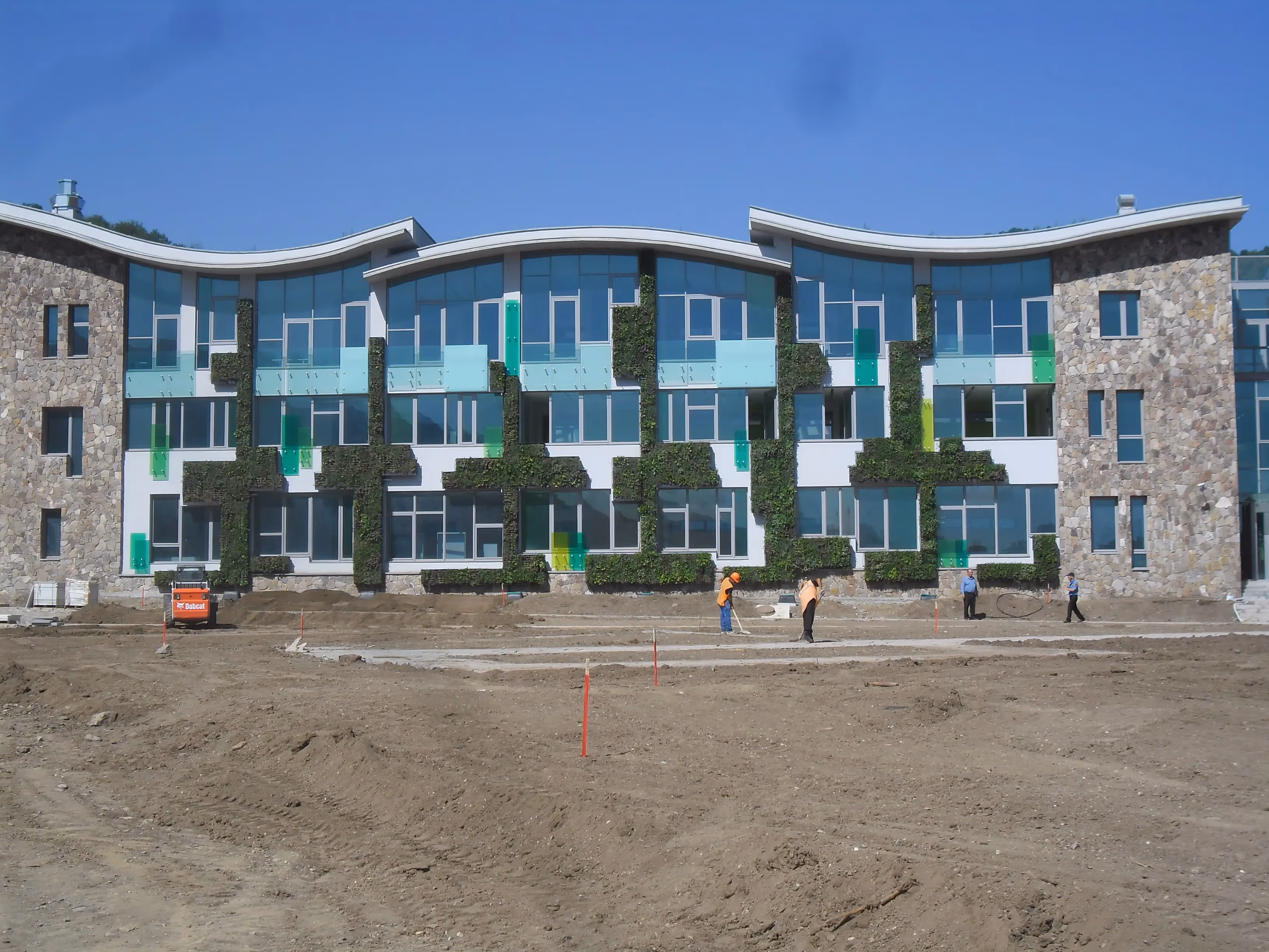 Modern building with green vertical gardens under construction on sunny day