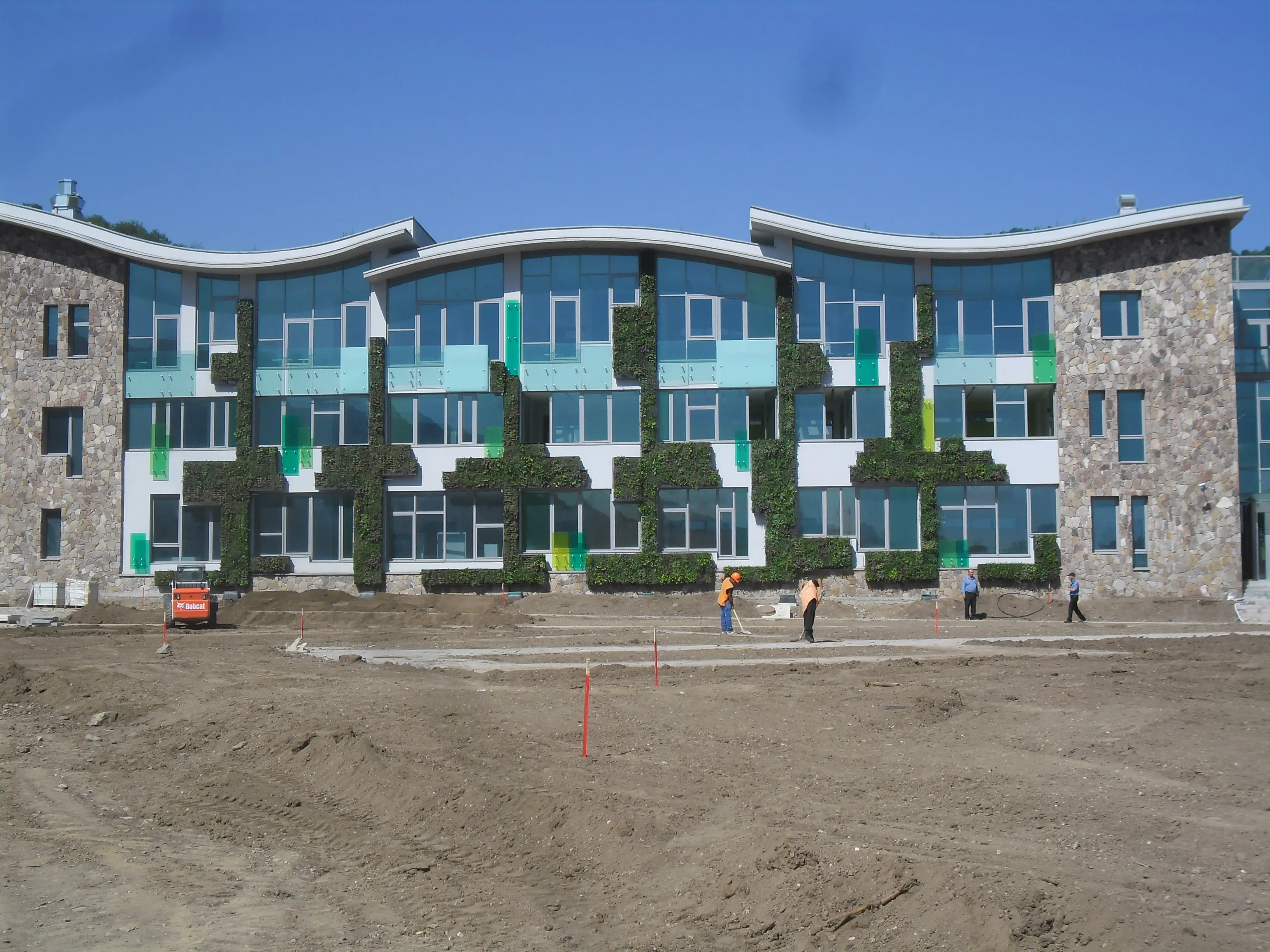 Modern building with green vertical gardens under construction on sunny day