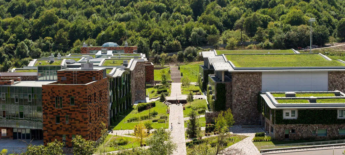 Modern eco-friendly campus with green roofs and stone buildings surrounded by forest