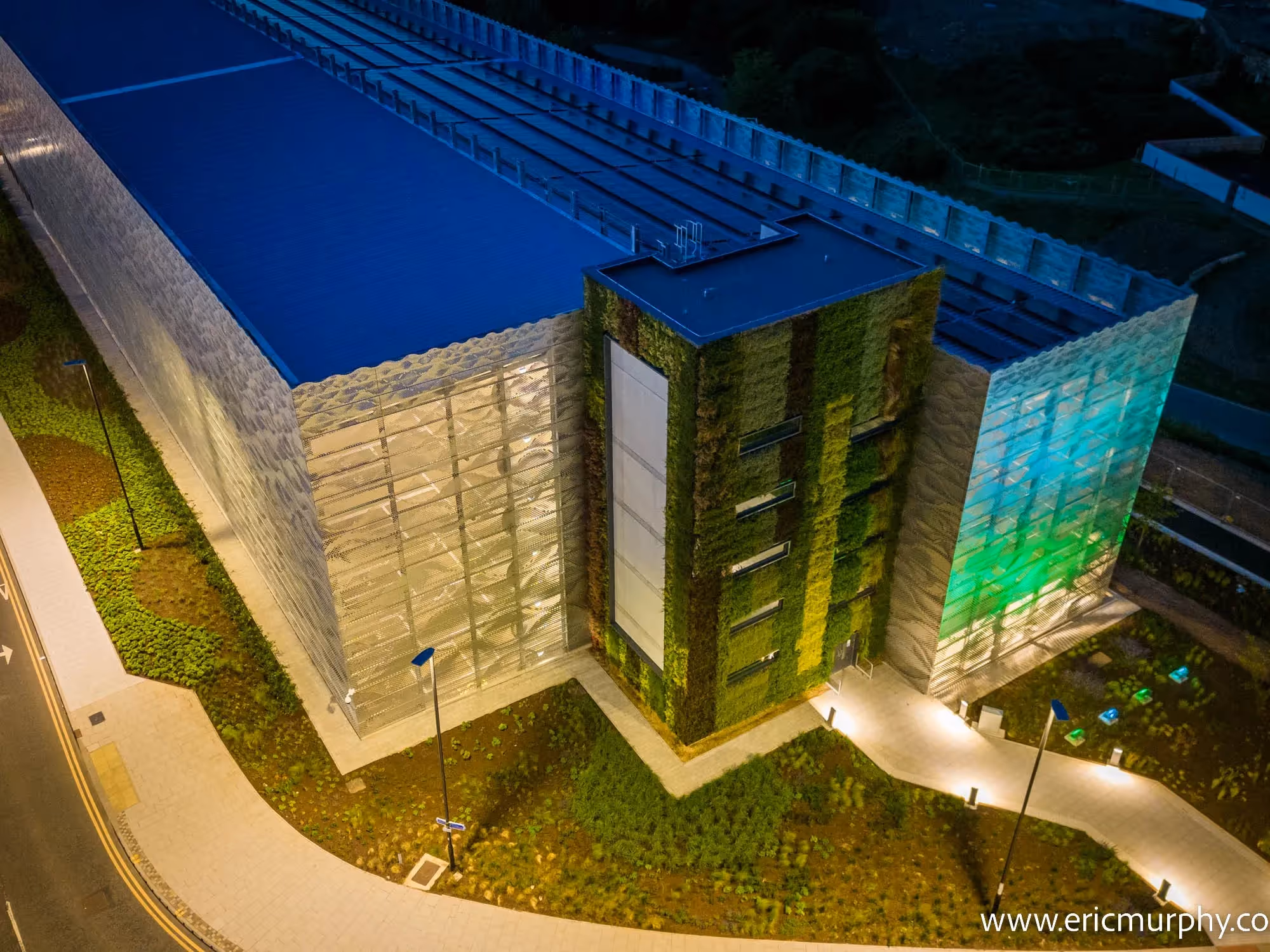 Modern green building with living walls at night, illuminated pathways