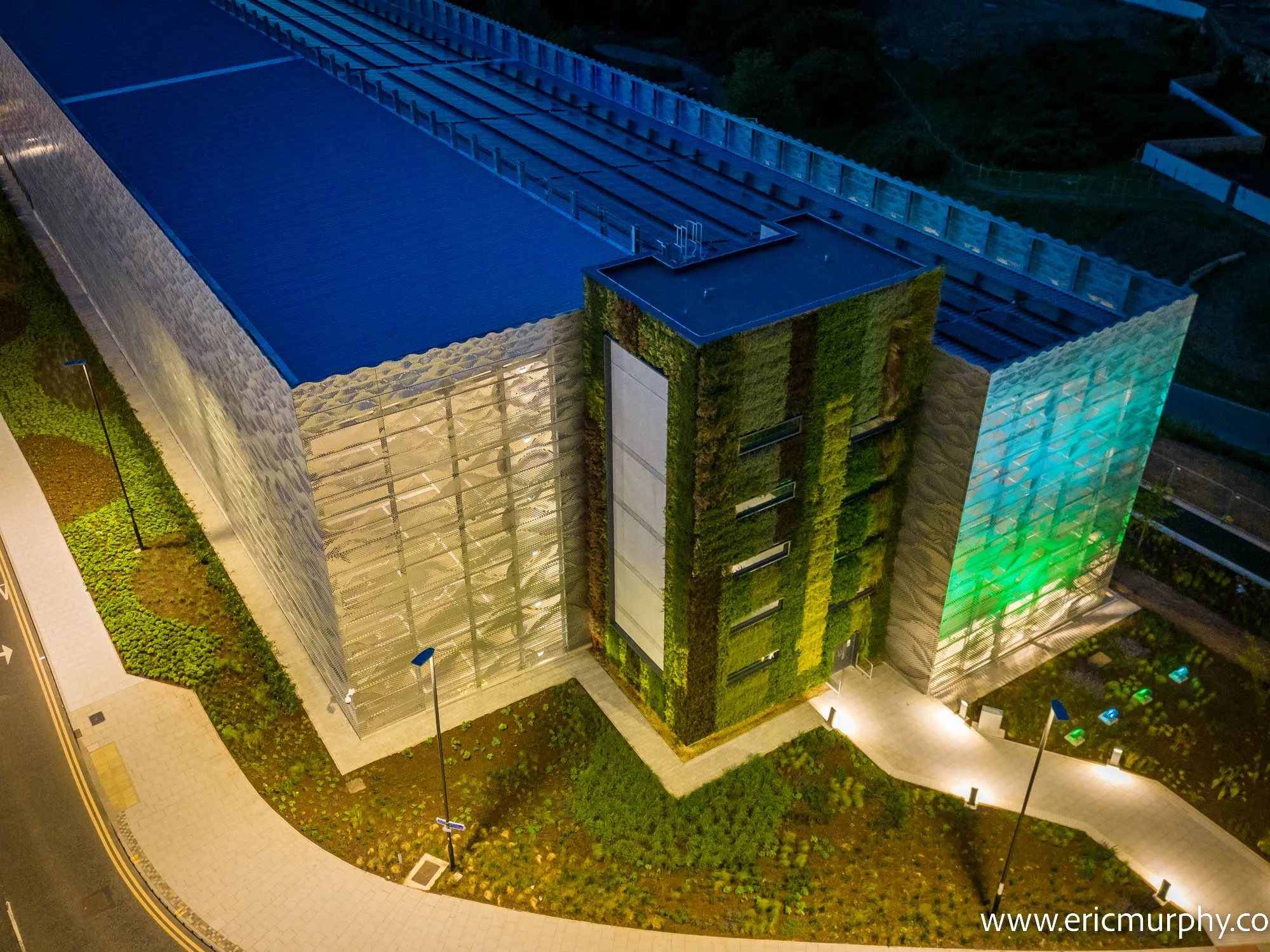 Modern green building with living walls at night, illuminated pathways