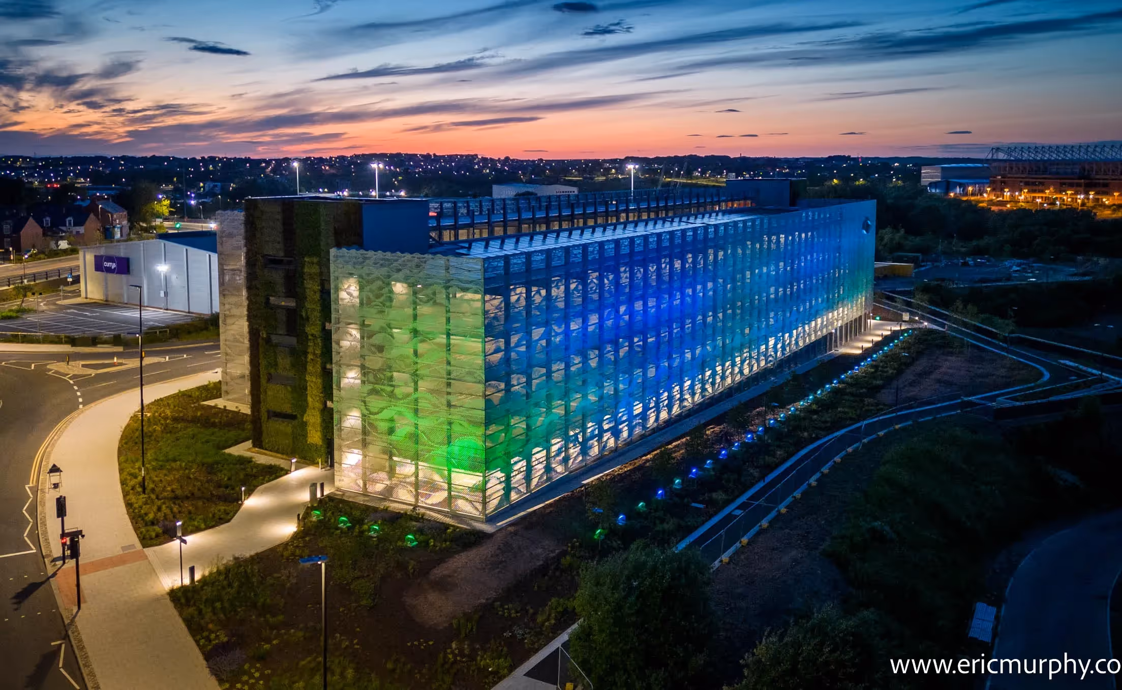 Modern glass office building illuminated at twilight with green and blue lights