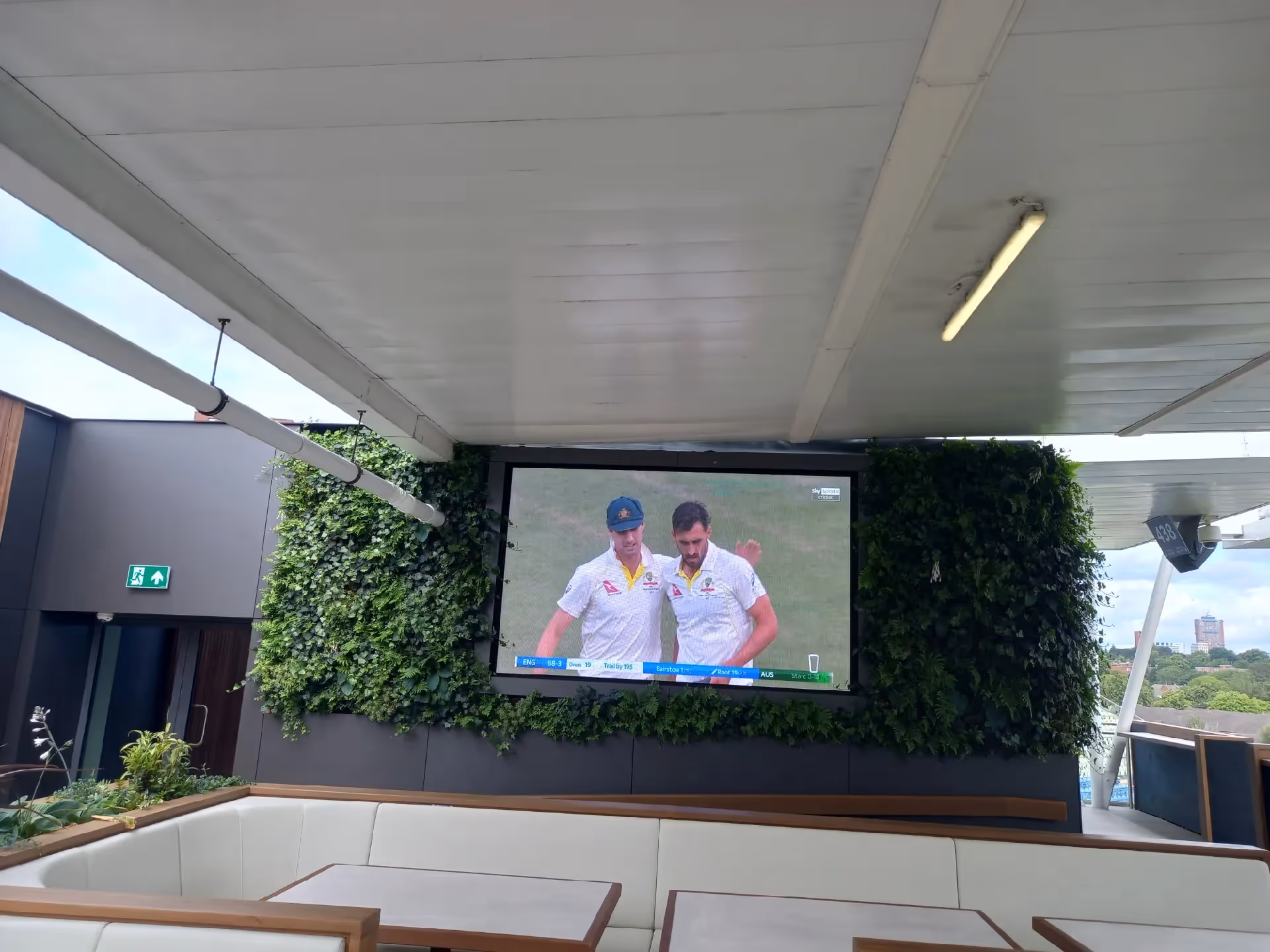 Cricket players on large screen surrounded by green living wall