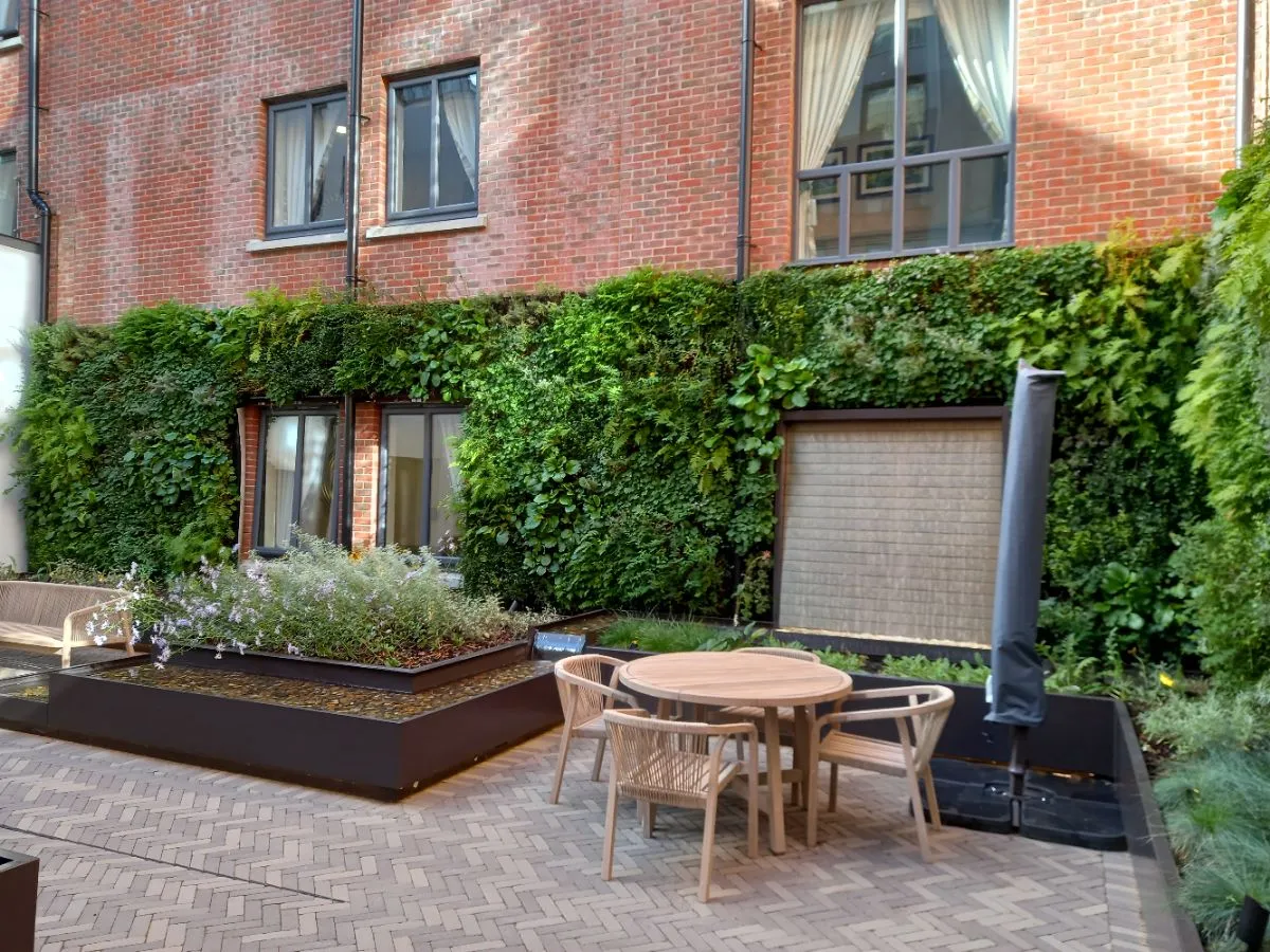 Urban patio with wooden furniture, green wall, and water feature