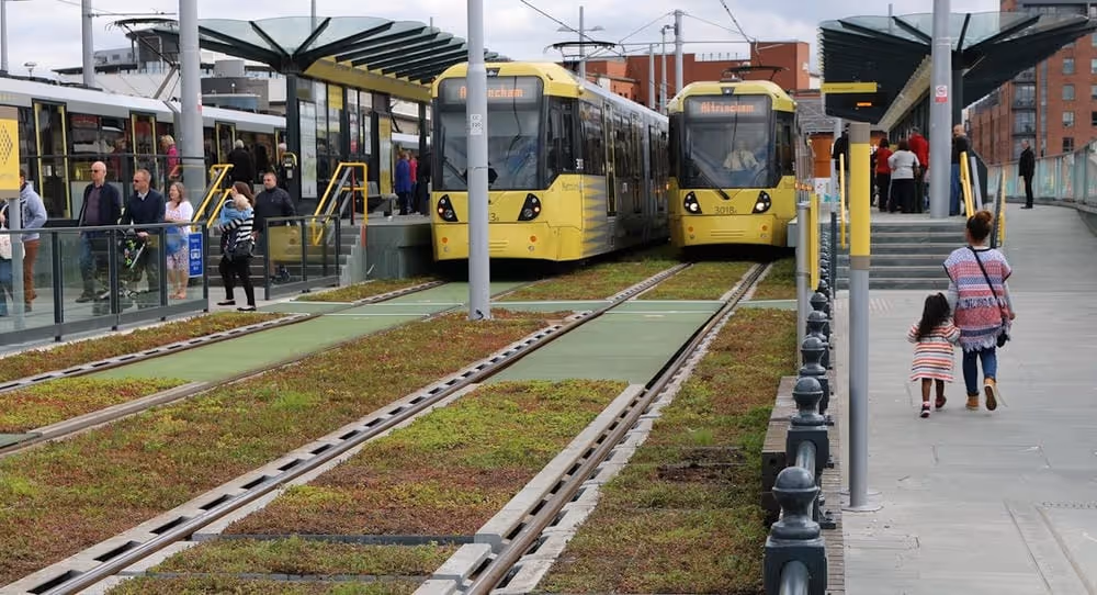 Castlefield Metrolink Station in Manchester, where two trains are stopped and between the tracks are spaces of green infrastructure