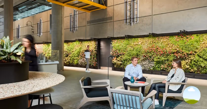 Interior of an office space with people talking and a large living wall along the back wall