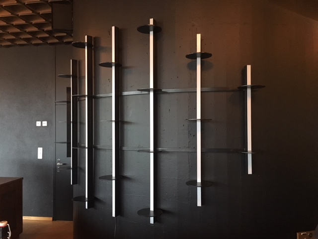 Minimalist black wall-mounted shelving unit with vertical white supports and small round shelves against a dark wall.