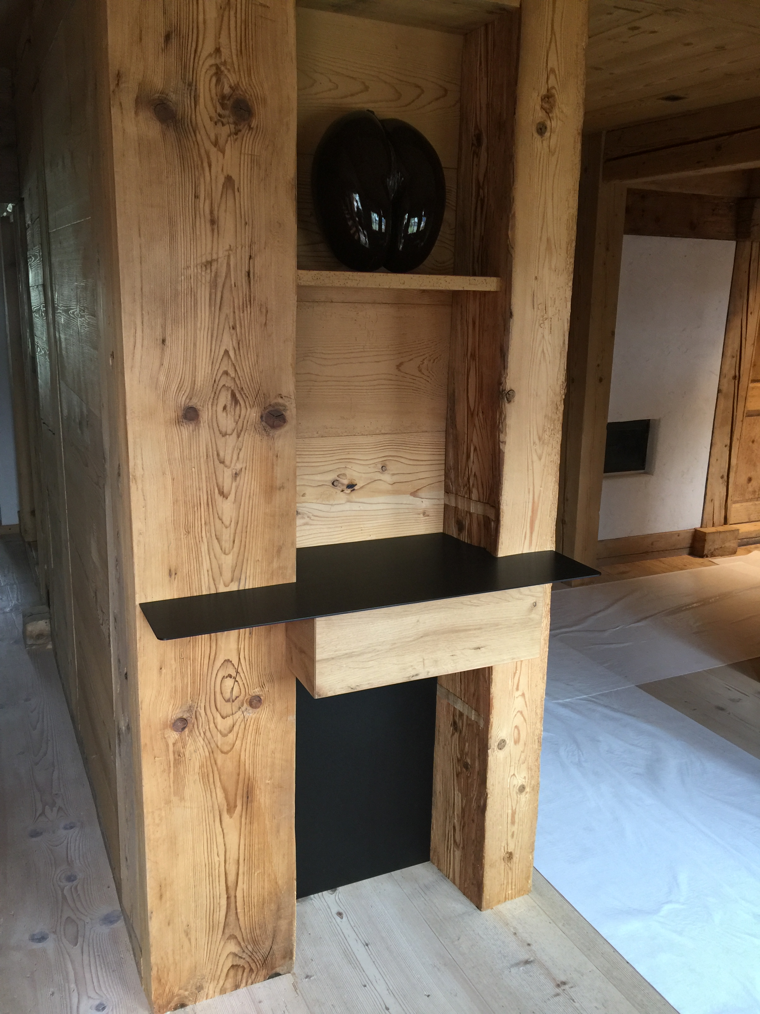 Wooden interior corner with integrated black floating shelf and small wooden drawer beneath.