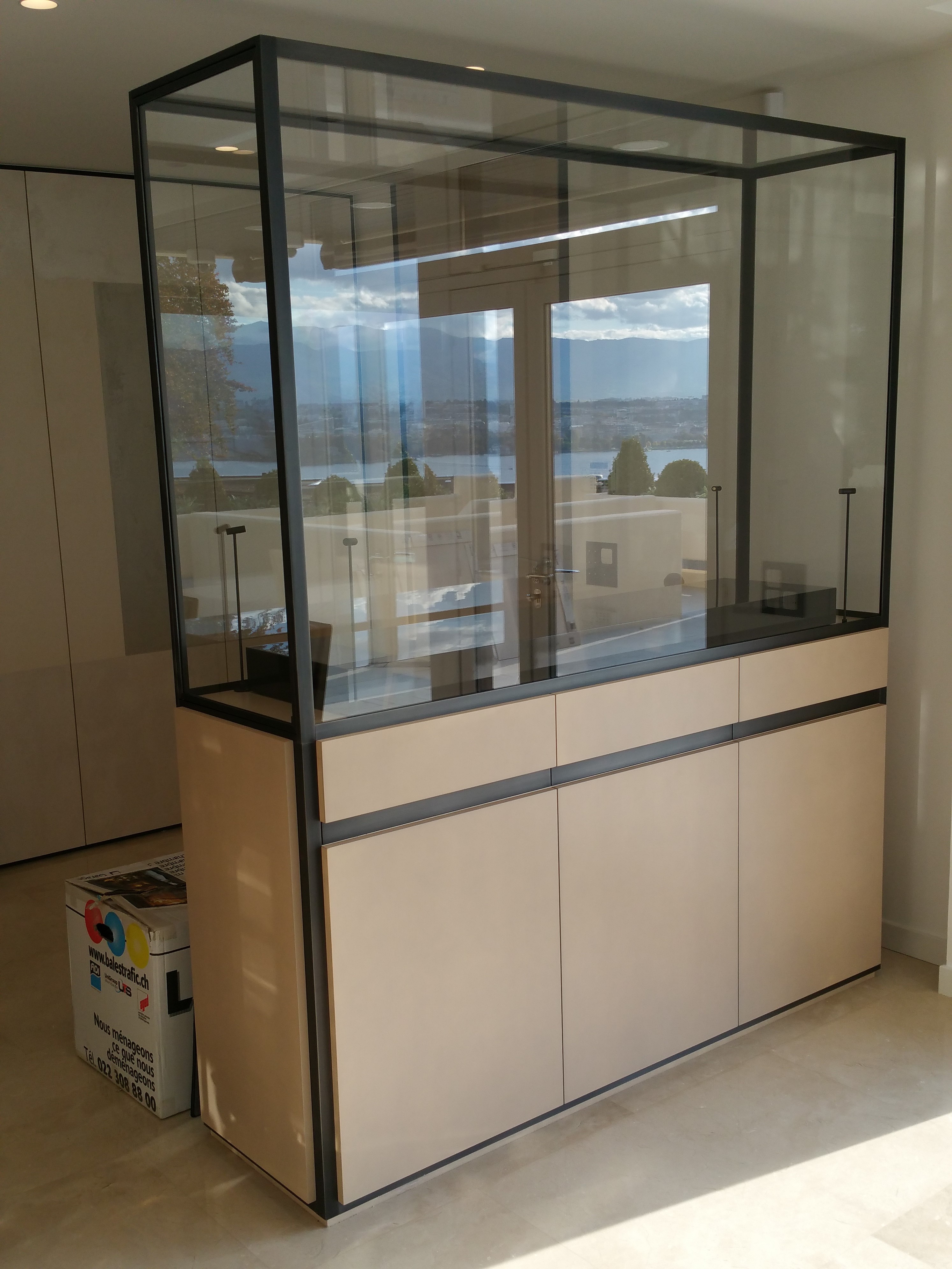 Modern display cabinet with glass upper section and beige lower cabinets in a bright room.