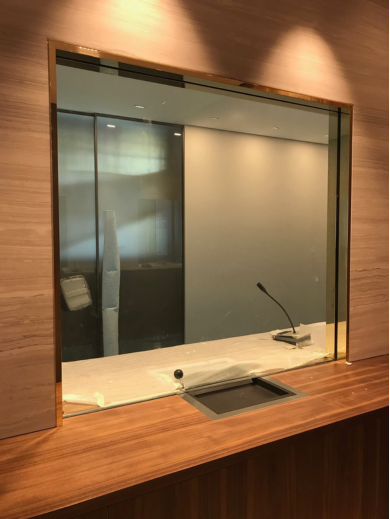 A reception window with a wooden ledge, a microphone, and a small opening beneath the glass for passing items.