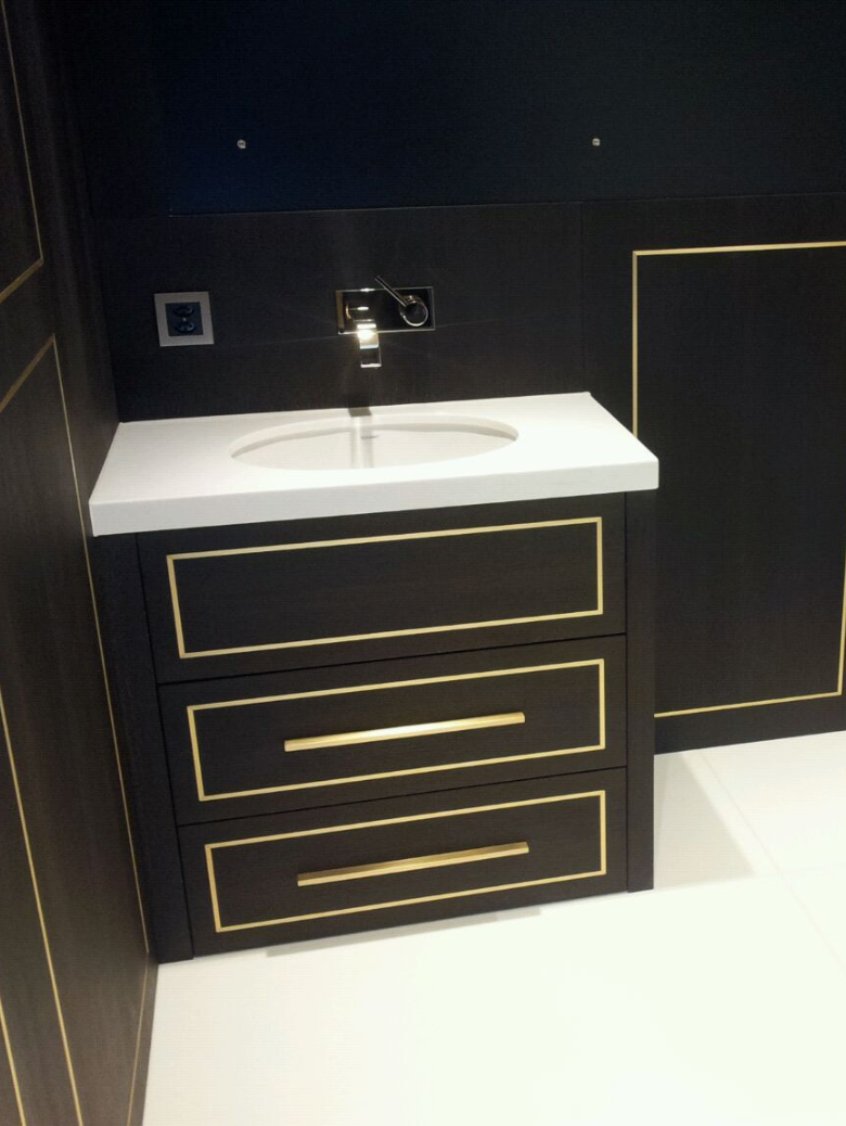 Modern black bathroom vanity with gold trim and white countertop with built-in sink and wall-mounted faucet.