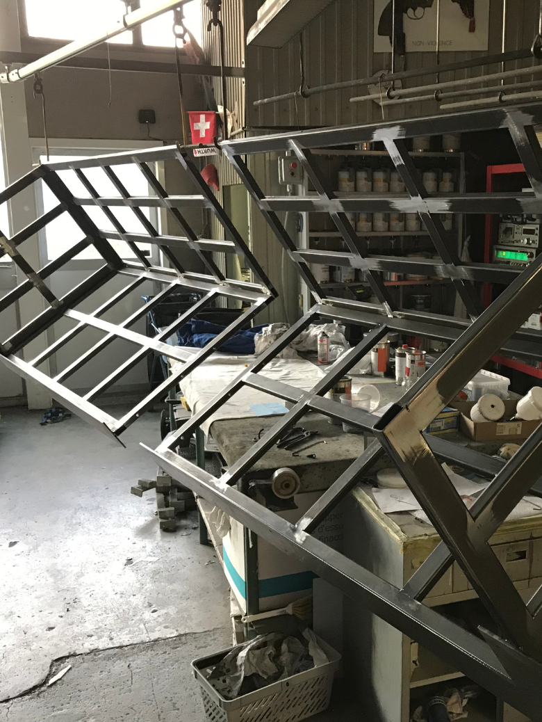 Metal frames with grid patterns hanging in a workshop with tools and paint cans on tables in the background.