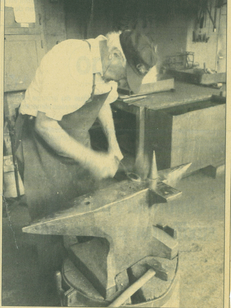 Blacksmith in workshop hammering a horseshoe on an anvil.