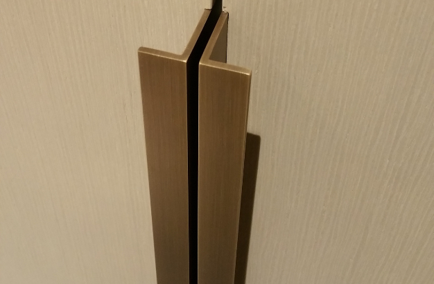 Close-up of two vertical bronze-colored door handles on a light textured wooden door.