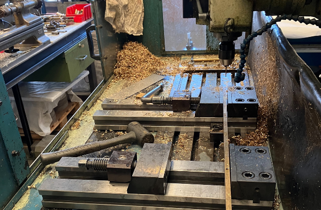 Metalworking machine with metal shavings and a hammer on the work surface inside a workshop.