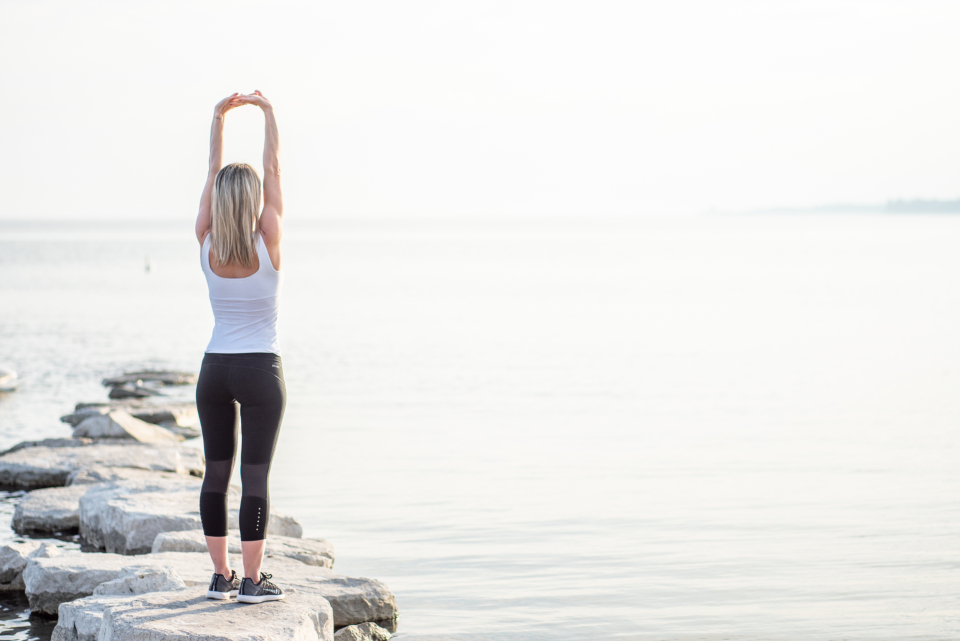 Woman stretching by the water in soft morning light