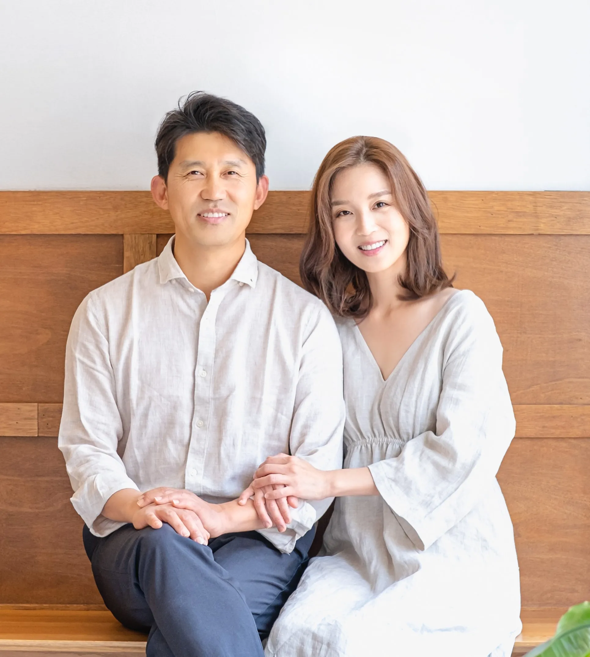 Portrait of Dr. Kyung Choi and Dr. Diana Lee, husband-and-wife dentists at Choi & Lee Family Dentistry in Chino, CA, sitting together and smiling warmly. Both are wearing light-colored clothing, creating a welcoming and approachable image that reflects their family-focused dental practice.