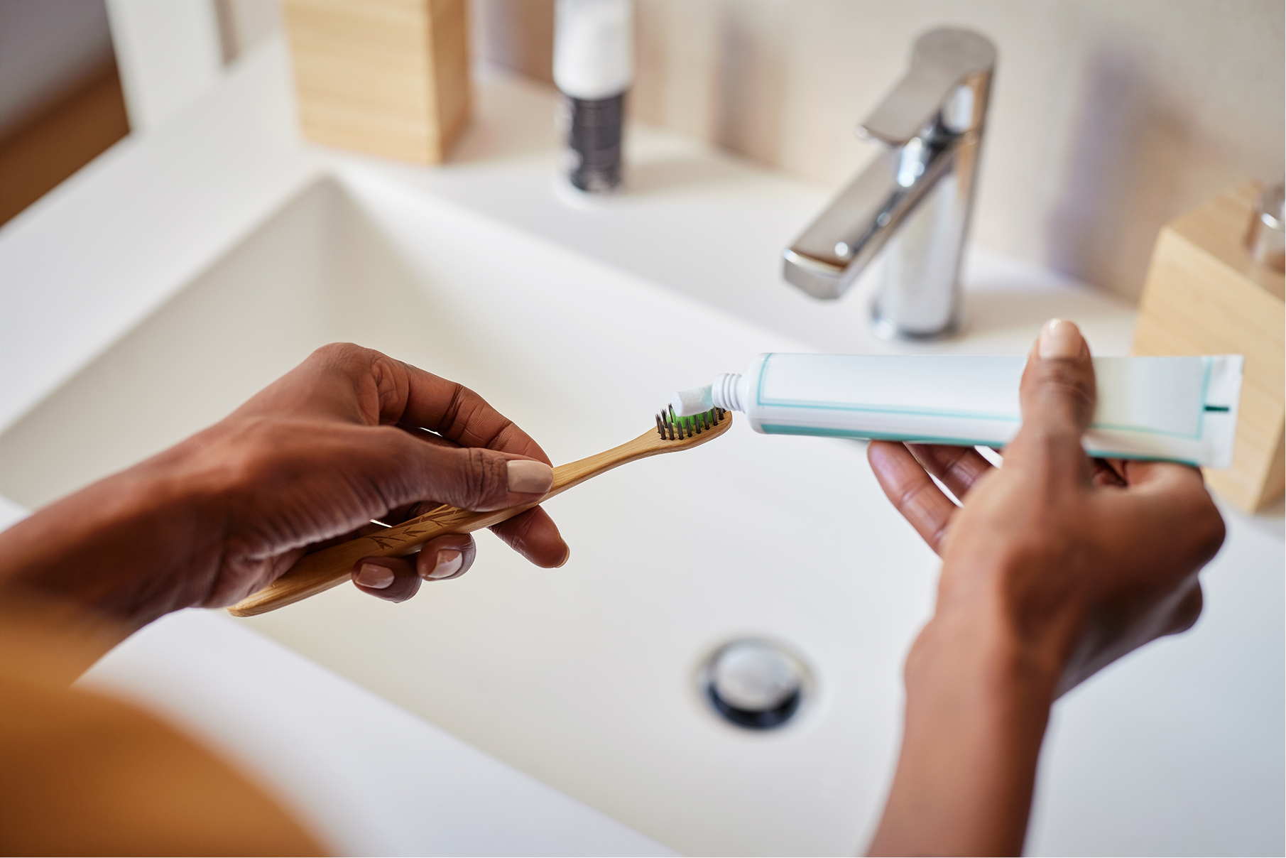 Close-up of hands applying toothpaste onto a toothbrush over a bathroom sink, preparing for daily oral hygiene.