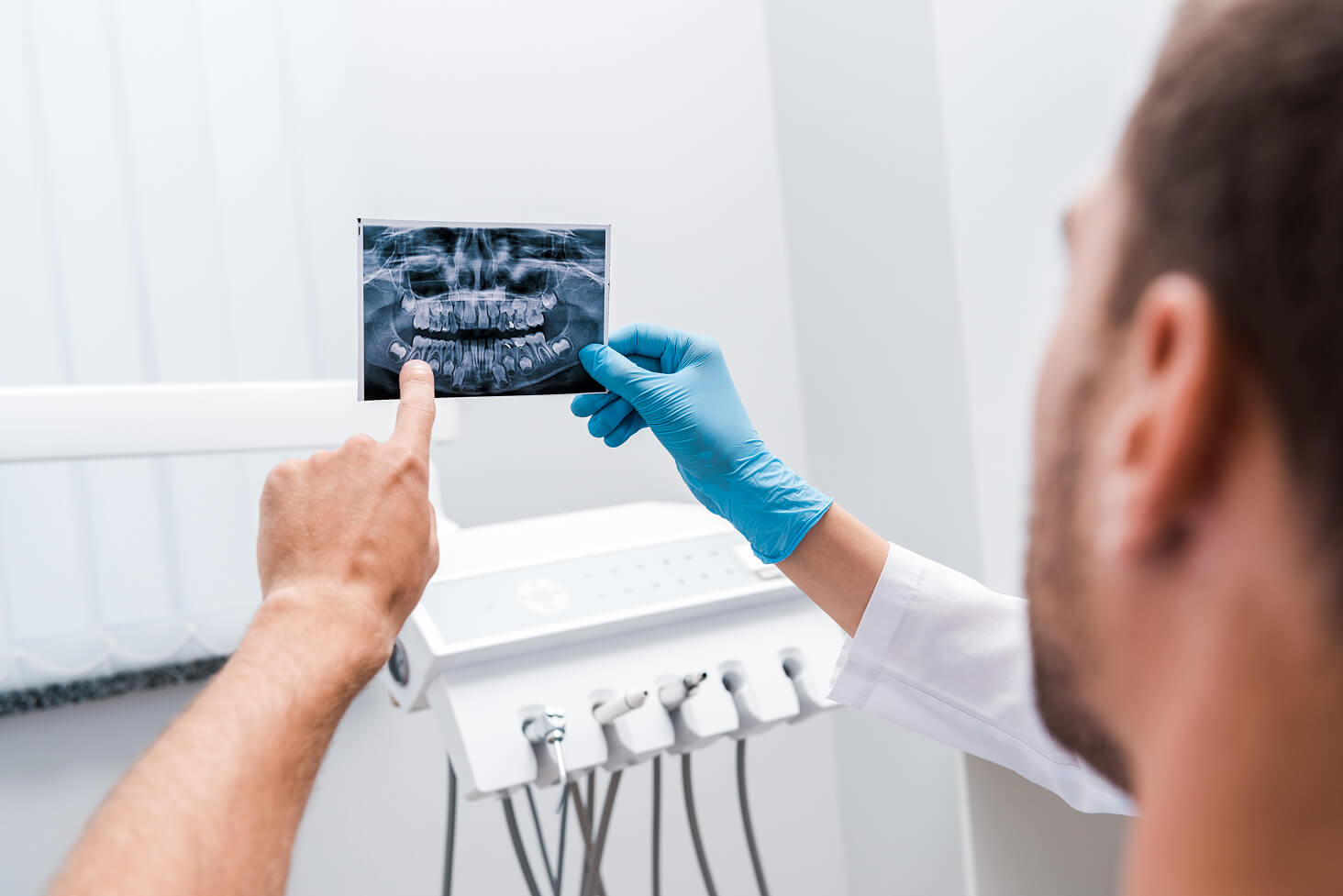Dentist wearing gloves holding a dental X-ray film in front of a patient during examination in a dental office.