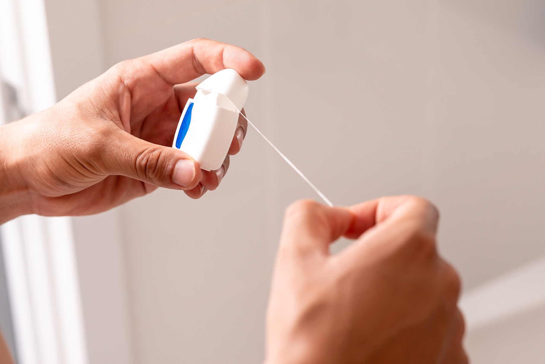 Close-up of hands pulling out dental floss from a container, showing proper preparation for flossing teeth.