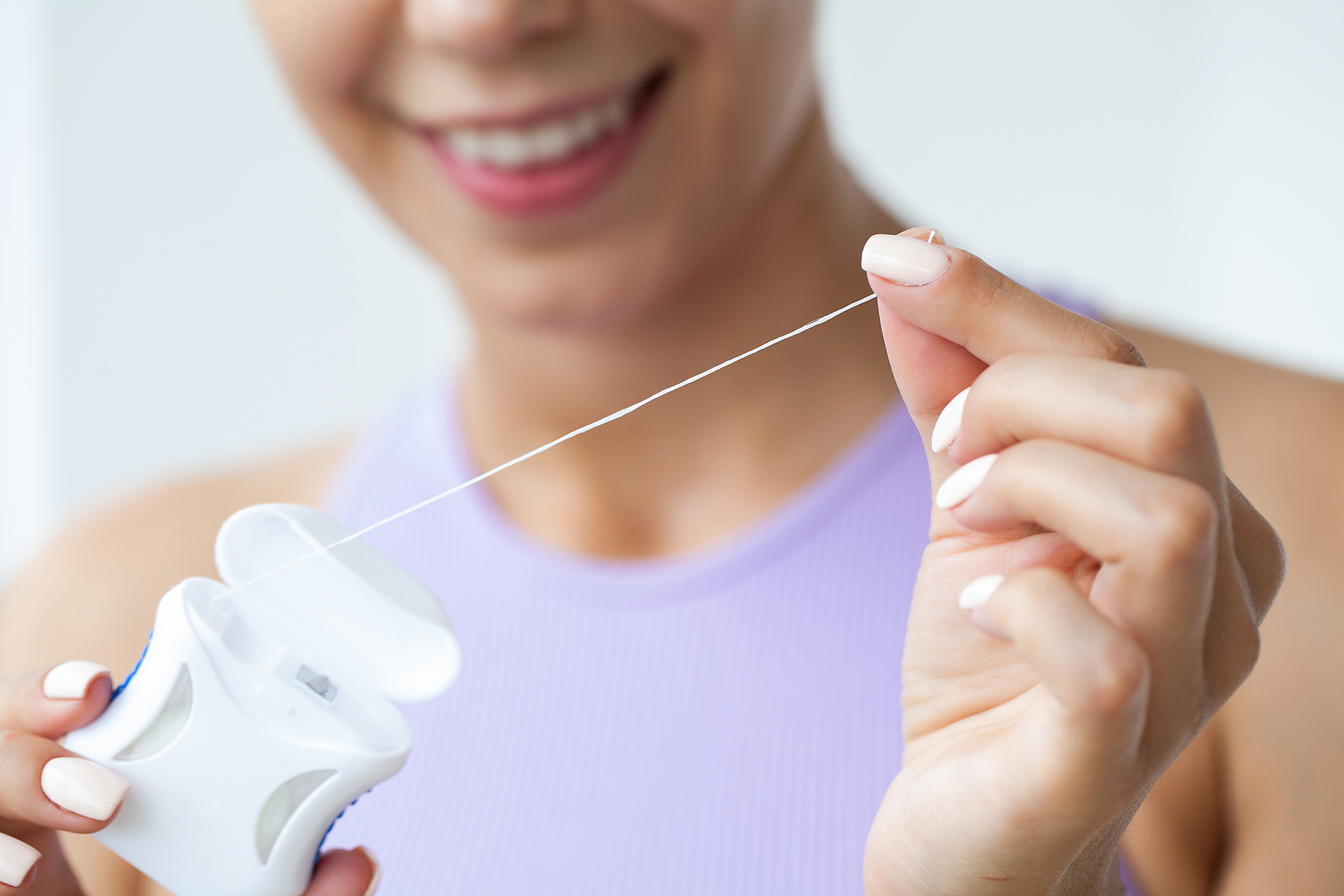 Smiling woman in a purple shirt holding a container of dental floss and preparing to floss her teeth.