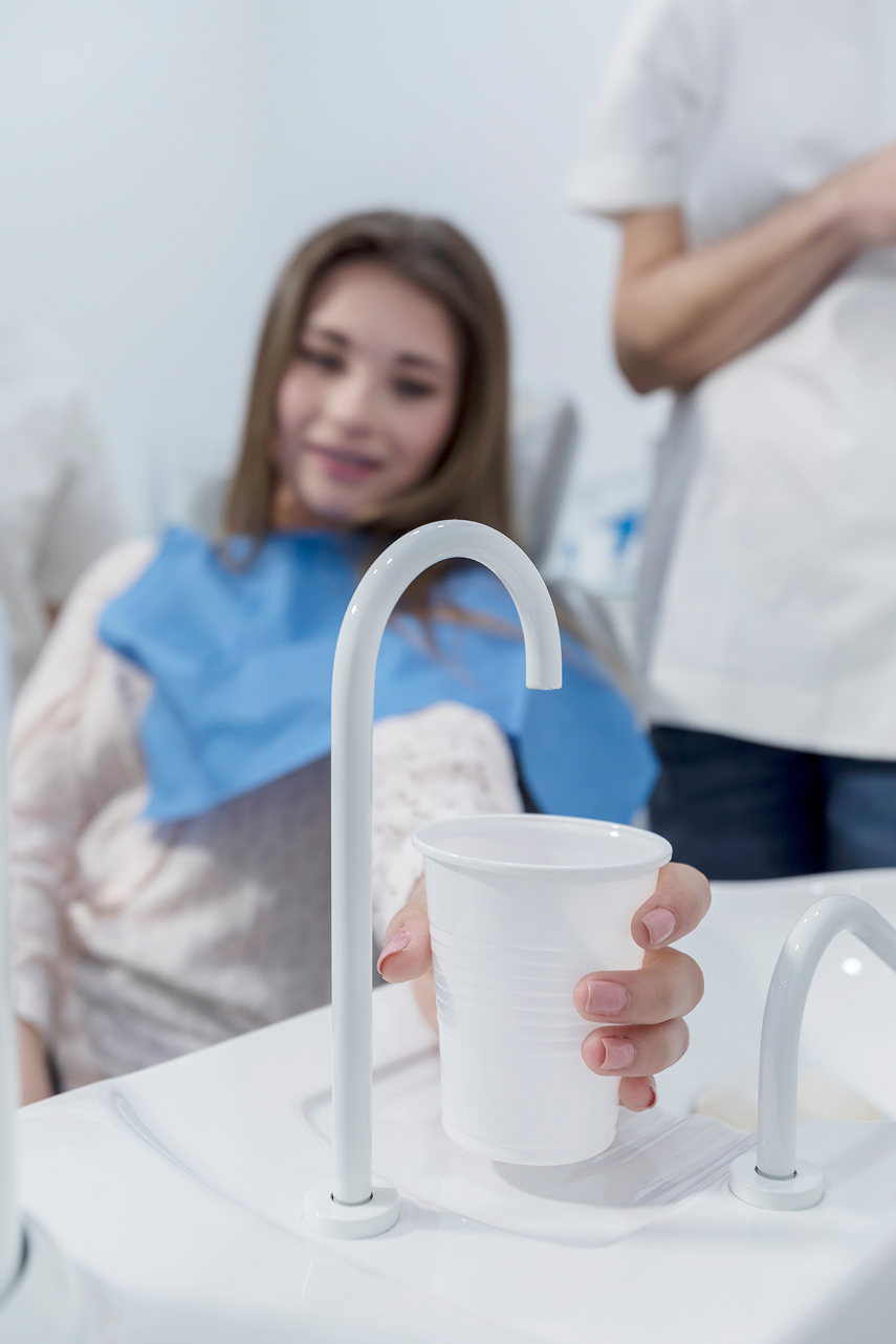Young female dental patient sitting in a chair, holding a cup and preparing to rinse her mouth after treatment.