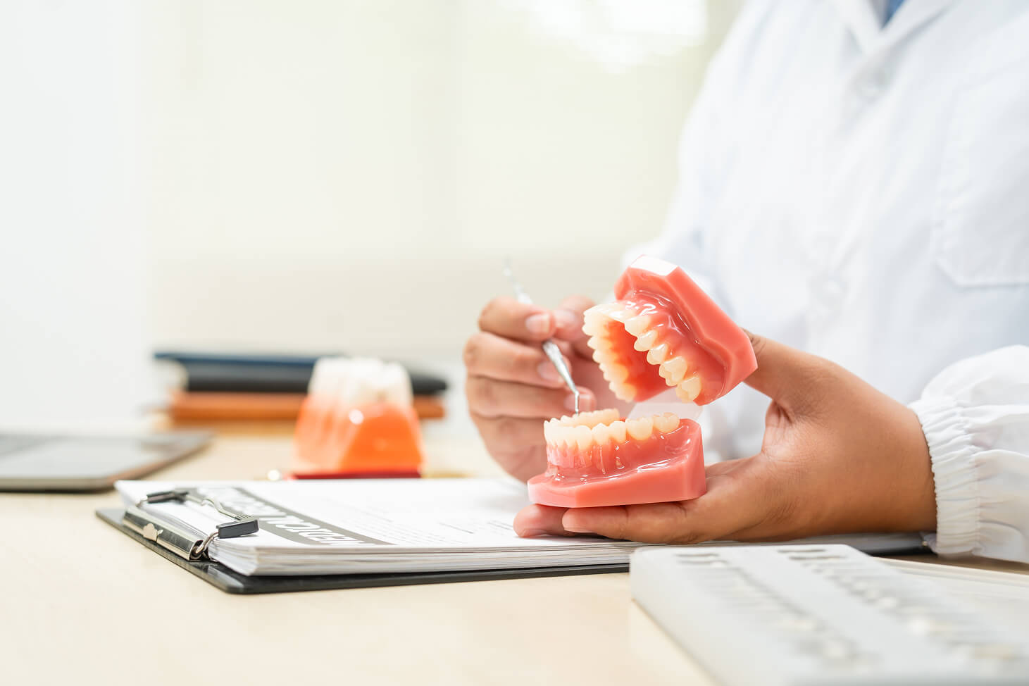 Dentist demonstrating dental procedures using a red and white model of human teeth on a desk during a consultation session.