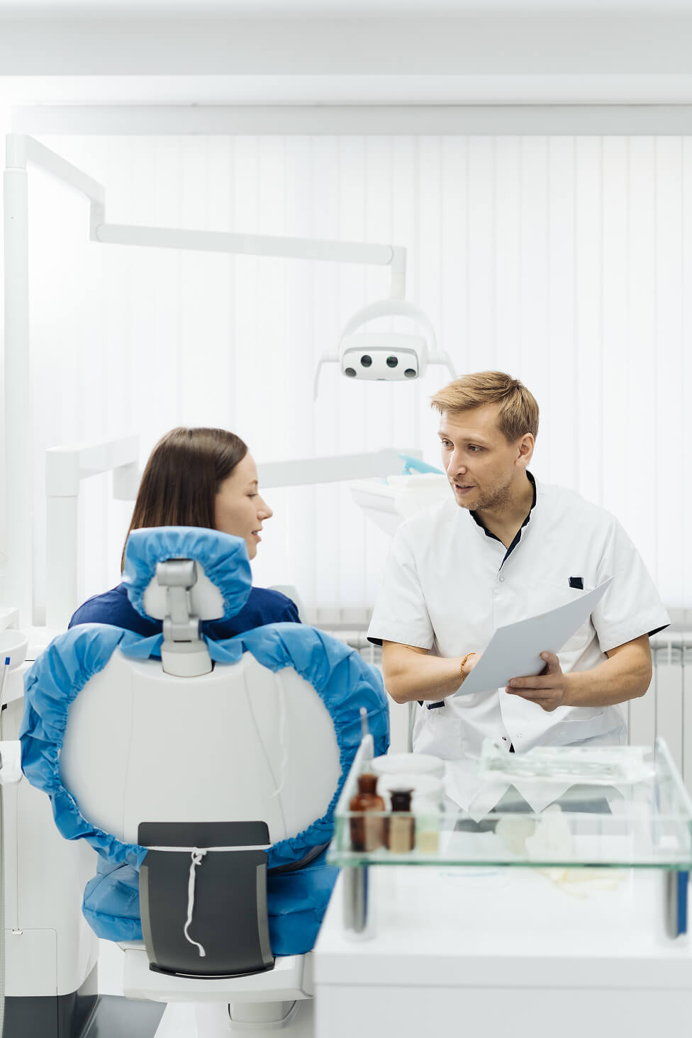 Dentist speaking with a patient seated in a chair, with dental equipment in the background during a checkup.