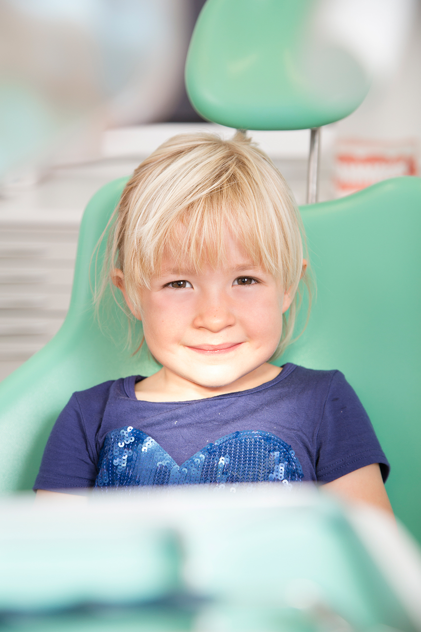 Young blonde girl sitting in a dental chair smiling after her pediatric dental checkup, showing comfort and confidence in the dentist’s office.