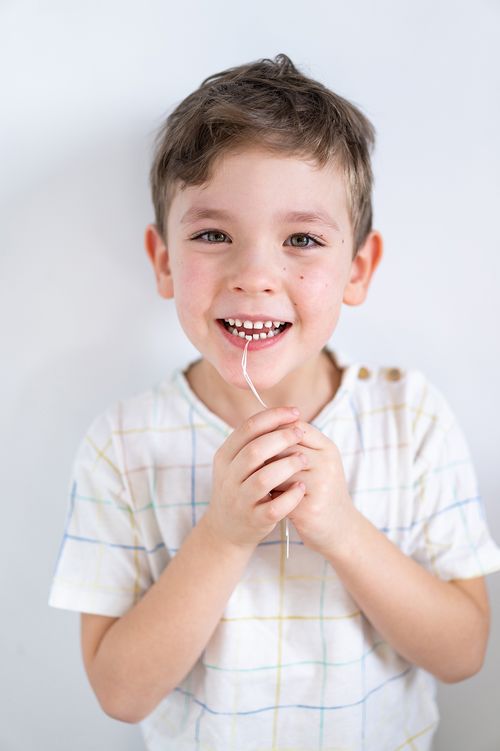 Smiling young boy holding dental floss in his hands, showing excitement about learning proper oral hygiene after a pediatric dental visit.
