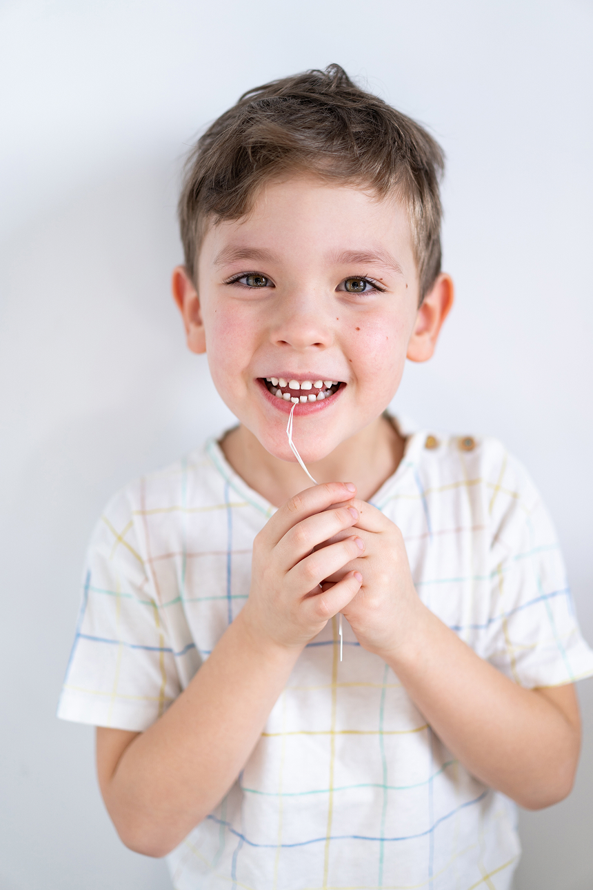 Smiling young boy holding dental floss in his hands, showing excitement about learning proper oral hygiene after a pediatric dental visit.
