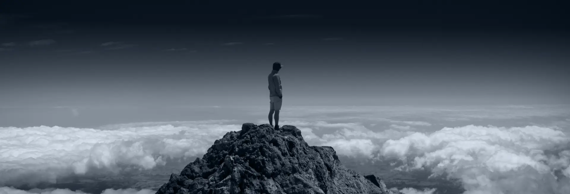 person standing on mountain top looking down at clouds
