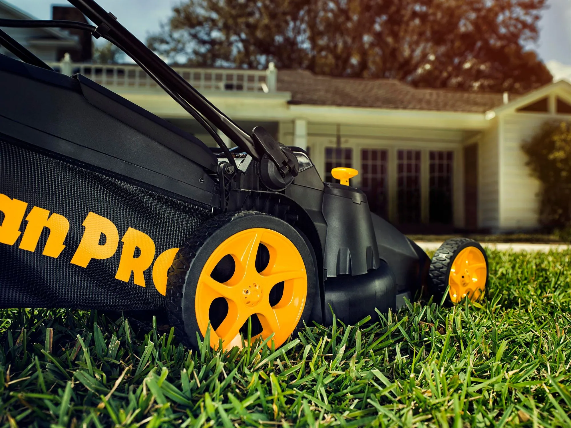 Close-up of the large, yellow rear wheel of a black Poulan Pro walk-behind lawn mower on a green lawn.