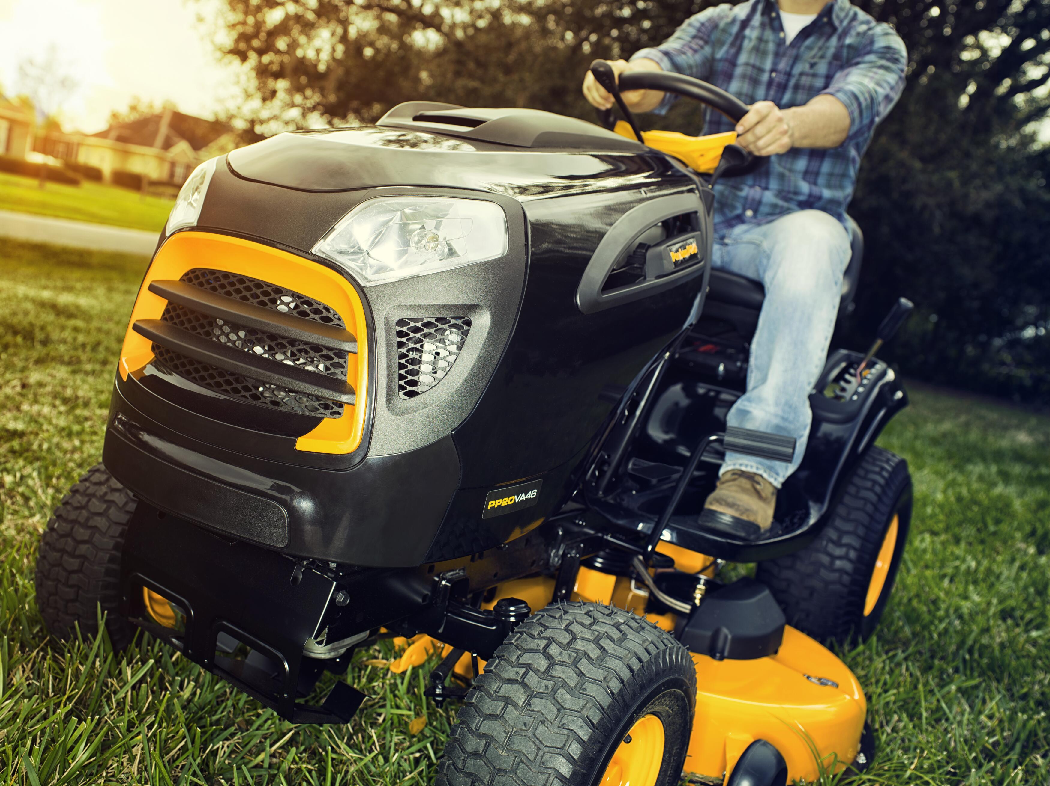Close-up of a Poulan Pro riding lawn mower being operated by a man on a green lawn.