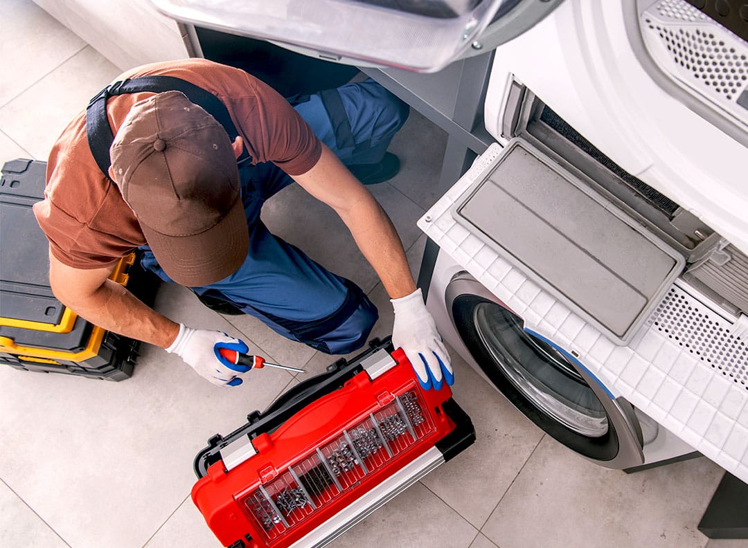 Mechanic sitting on the floor fixing something in the laundry room.
