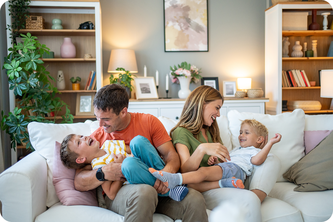 Family with 2 young kids sitting on the couch and laughing. 