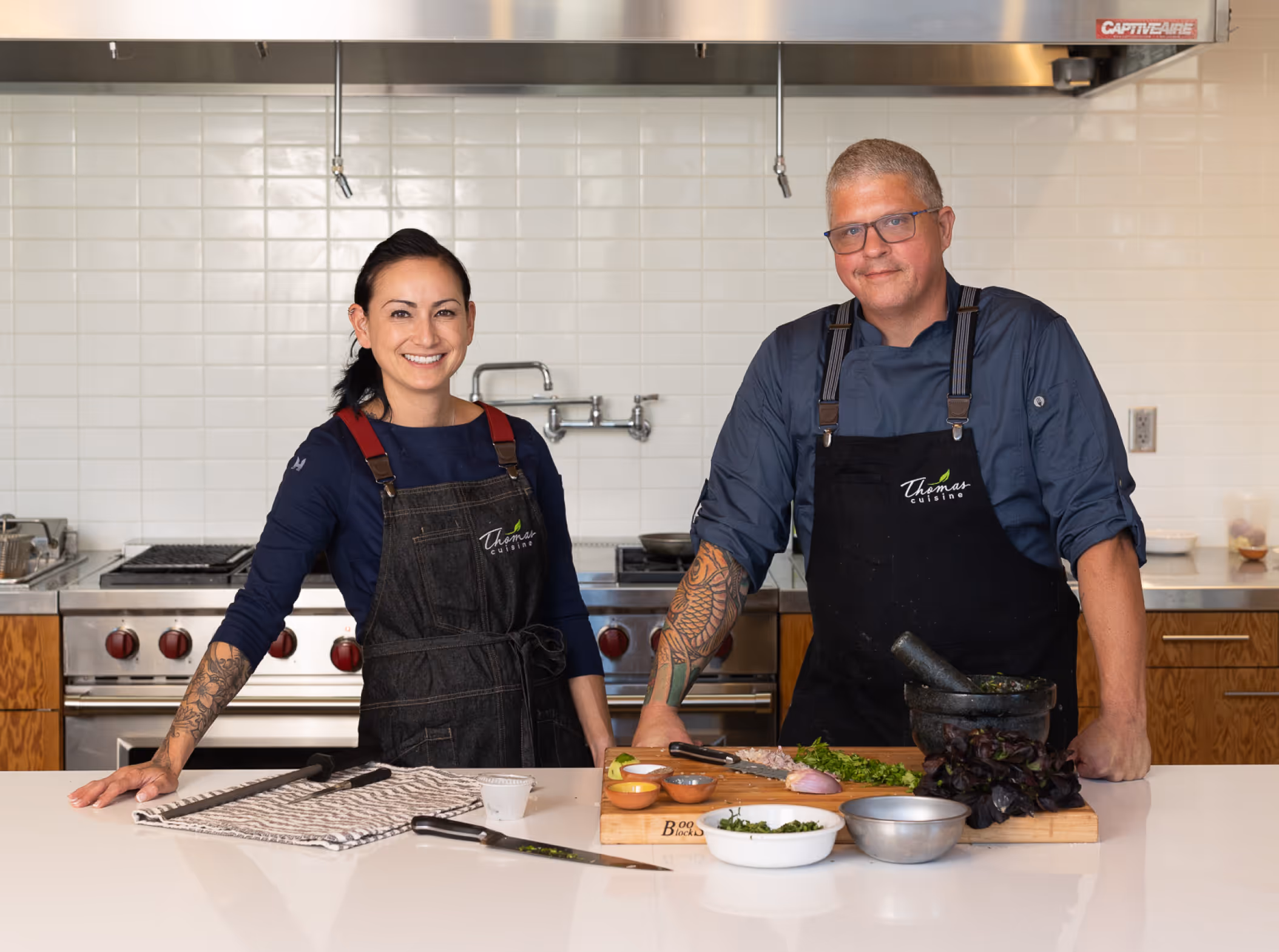 Person in a Thomas Cuisine apron and blue gloves sprinkling flour on a mound of orange dough on a wooden board.